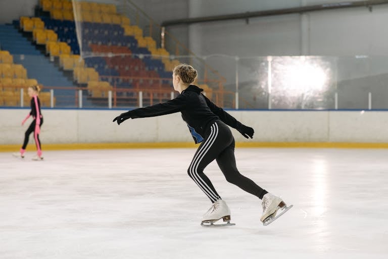 Action shot of a figure skater in motion at an indoor ice rink, showcasing athletic grace and balance.