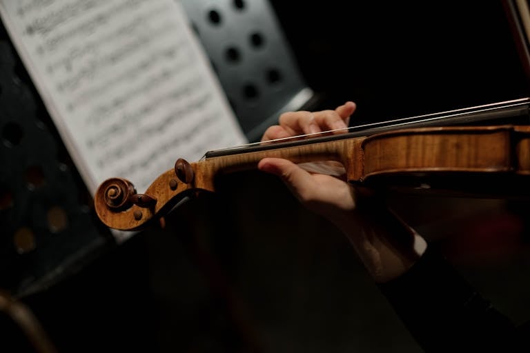 Close-up of a hand playing a violin with a sheet music stand in the background.